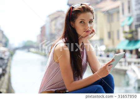 Beautiful woman sitting outdoors and using a tablet watching med Beautiful woman sitting outdoors and using a tablet watching med 31657850