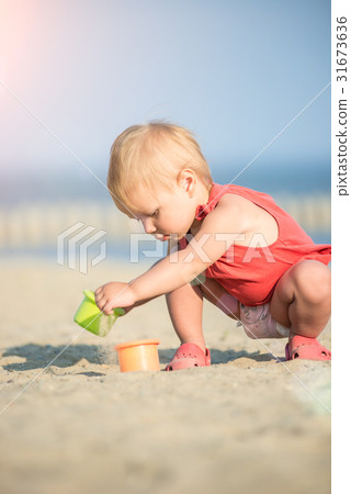 Baby girl in red dress playing on sandy beach near 31673636