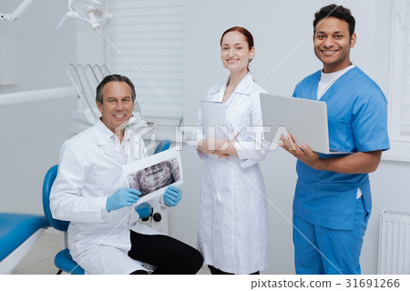 Friendly team of three dentists posing on camera Friendly team of three dentists posing on camera 31691266