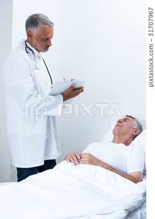 Male doctor writing medical report of senior man on clipboard 31707967