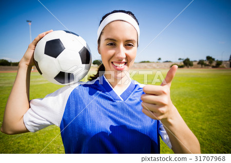Happy soccer player holding a ball and showing her thumbs up 31707968