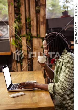Hipster drinking a cup of coffee while using a laptop Hipster drinking a cup of coffee while using a laptop 31709376