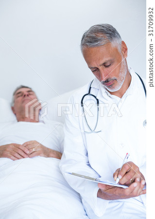 Male doctor writing medical report of senior man on clipboard 31709932