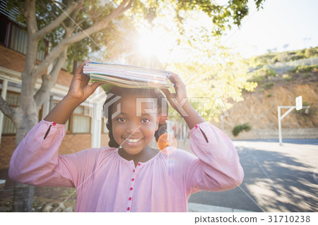 Schoolgirl carrying books on her head 31710238