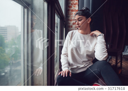 Attractive woman in gray sweatshirt sits on window Attractive woman in gray sweatshirt sits on window 31717618