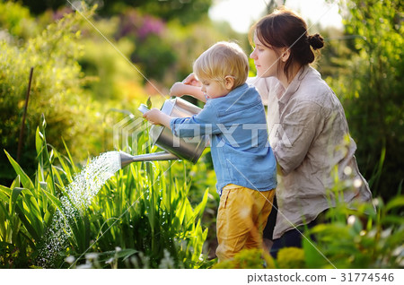Cute toddler boy and his young mother watering plants in the garden Cute toddler boy and his young mother watering plants in the garden 31774546