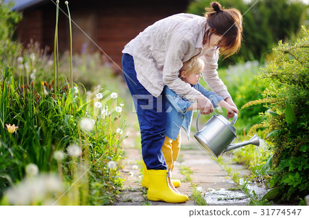 Cute toddler boy and his young mother watering plants in the garden 31774547