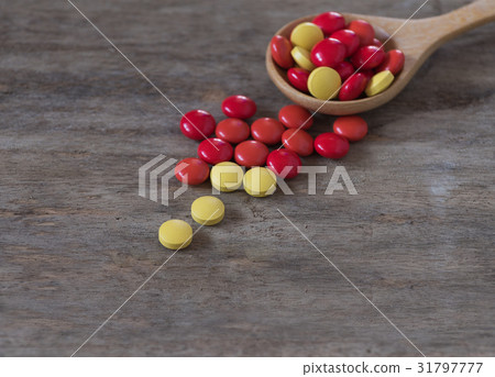 Red yellow pills and wood spoon on wood 31797777