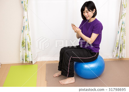 A woman sitting on a balance ball and playing with a smartphone A woman sitting on a balance ball and playing with a smartphone 31798695