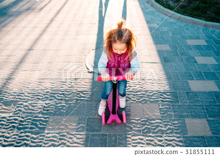 Little girl with blonde hair rides on scooter 31855111