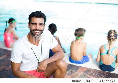 Male instructor crouching by children at poolside Male instructor crouching by children at poolside 31877231