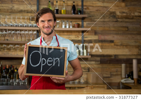 Happy barista holding open signboard in coffee shop Happy barista holding open signboard in coffee shop 31877327