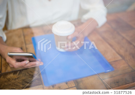 Woman holding coffee cup and mobile phone seen through cafe window 31877526