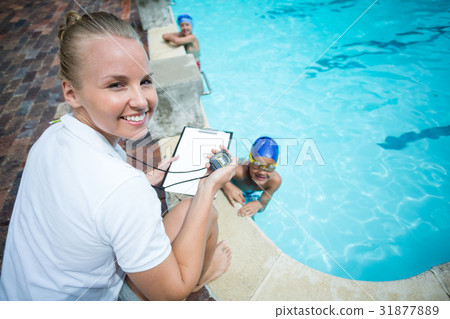 Instructor monitoring time of children swimming in pool 31877889