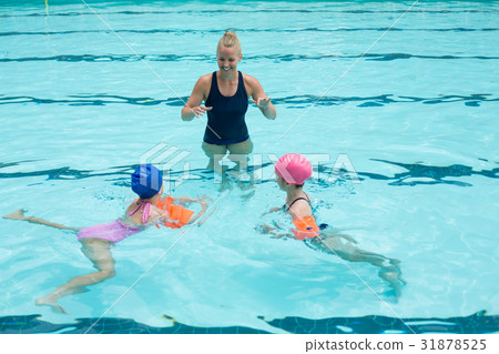 Happy instructor assisting children in swimming pool 31878525