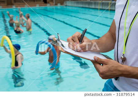Swim coach writing on clipboard near poolside Swim coach writing on clipboard near poolside 31879514