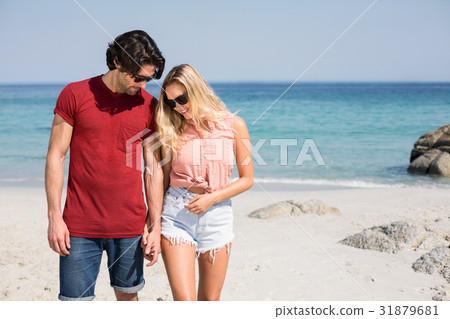 Couple wearing sunglasses while standing at beach Couple wearing sunglasses while standing at beach 31879681