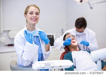 Portrait of smiling dentist standing while her colleague examining patient in background 31879807