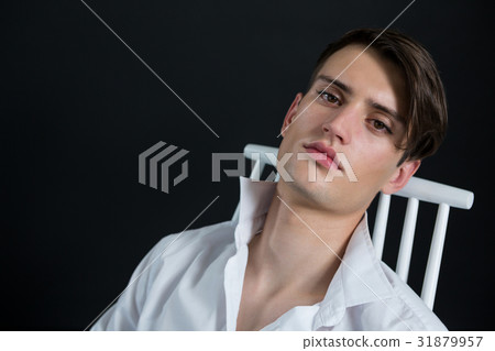 Androgynous man posing while sitting on chair 31879957