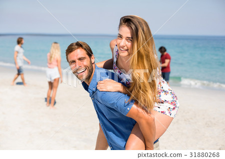 Man piggybacking girlfriend against friends at beach Man piggybacking girlfriend against friends at beach 31880268