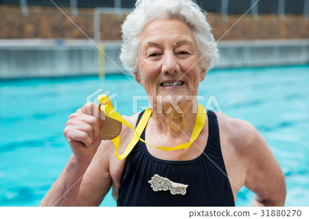 Senior woman showing gold medal at poolside Senior woman showing gold medal at poolside 31880270