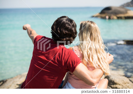 Man pointing towards sea while sitting with woman 31880314