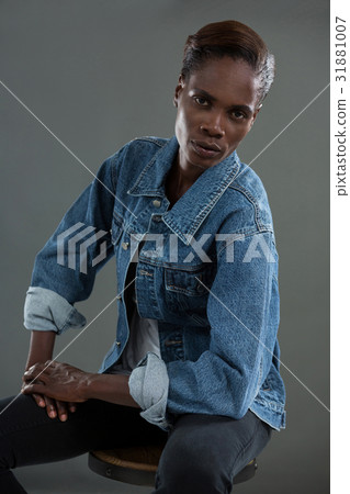 Androgynous man in denim jacket posing against grey background 31881007