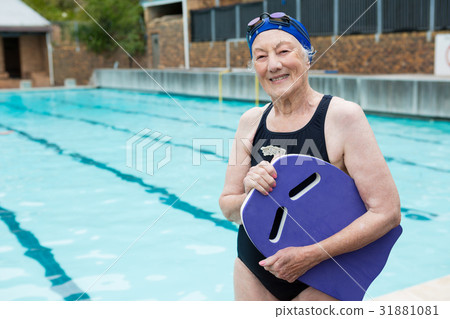 Smiling senior woman holding kickboard at poolside 31881081