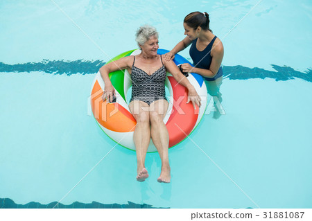 Trainer assisting senior woman on inflatable ring in swimming pool Trainer assisting senior woman on inflatable ring in swimming pool 31881087