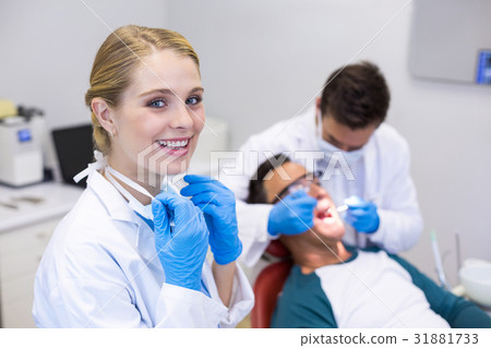 Portrait of smiling dentist standing while her colleague examining patient in background 31881733