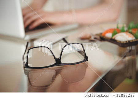 Eyeglasses on table against woman using laptop 31882282