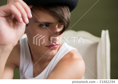 Androgynous man in hat sitting on chair 31882294