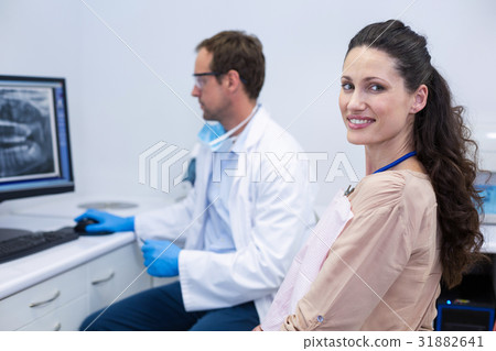 Female patient smiling at camera while dentist looking at an x-ray Female patient smiling at camera while dentist looking at an x-ray 31882641