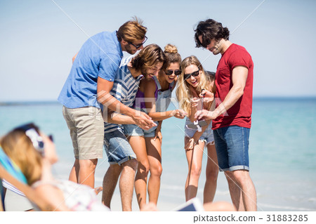Friends gesturing while looking in mobile phone at beach Friends gesturing while looking in mobile phone at beach 31883285