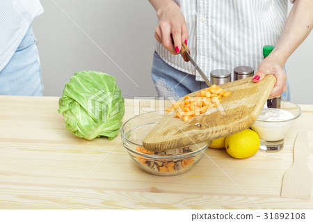 Female hands chop fresh carrot for salad on board Female hands chop fresh carrot for salad on board 31892108