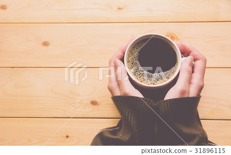 Female hands holding a cup of coffee over table Female hands holding a cup of coffee over table 31896115