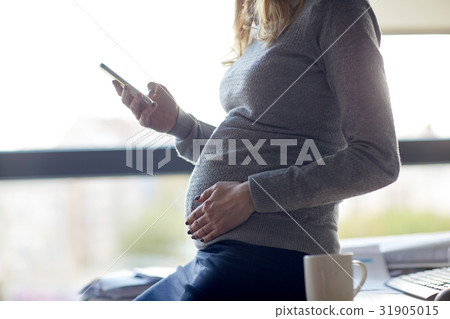 pregnant businesswoman with smartphone at office 31905015