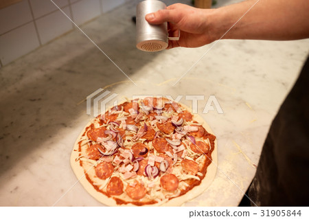 cook adding pepper to salami pizza at pizzeria 31905844