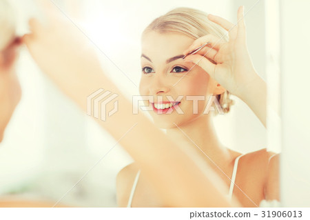 woman with tweezers tweezing eyebrow at bathroom 31906013