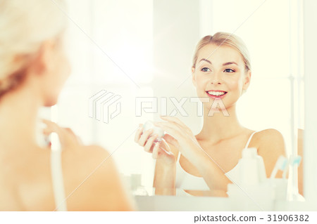 happy woman applying cream to face at bathroom 31906382
