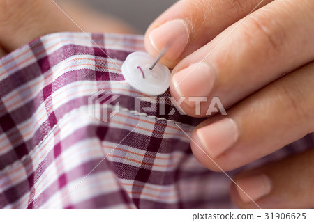 woman with needle stitching on button to shirt woman with needle stitching on button to shirt 31906625