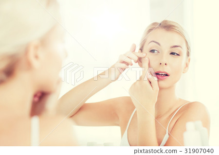 woman squeezing pimple at bathroom mirror 31907040