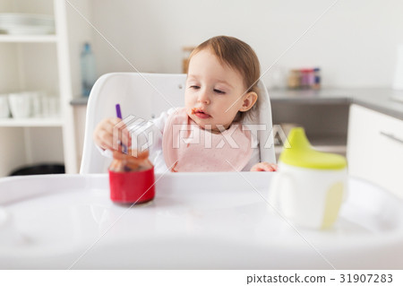 baby girl with spoon eating puree from jar at home 31907283