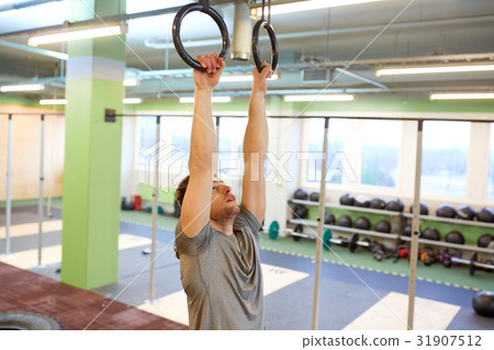 man exercising and doing ring pull-ups in gym 31907512