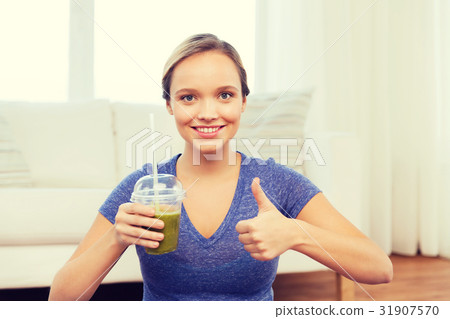 happy woman with cup of smoothie showing thumbs up 31907570