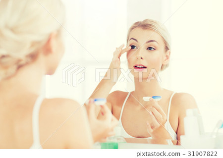 young woman putting on contact lenses at bathroom 31907822
