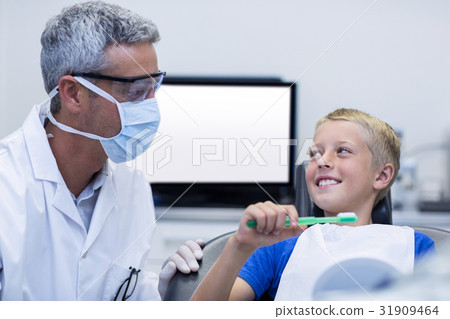 Dentist assisting young patient while brush teeth Dentist assisting young patient while brush teeth 31909464