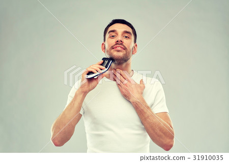 smiling man shaving beard with trimmer over gray smiling man shaving beard with trimmer over gray 31910035