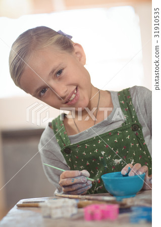Smiling girl painting on bowl in pottery workshop 31910535