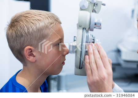 Young patient under going eye test through phoropter Young patient under going eye test through phoropter 31946084